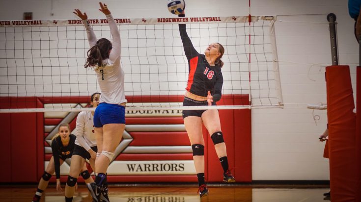 Ridgewater volleyball player spikes ball over net while opposing player attempts to block