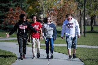 three male students and one female student walking on campus