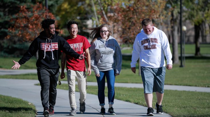 three male students and one female student walking on campus