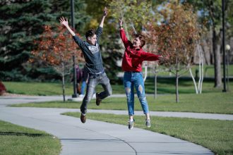 Two students jumping in the air on a sidewalk