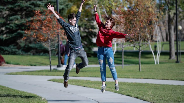 Two students jumping in the air on a sidewalk