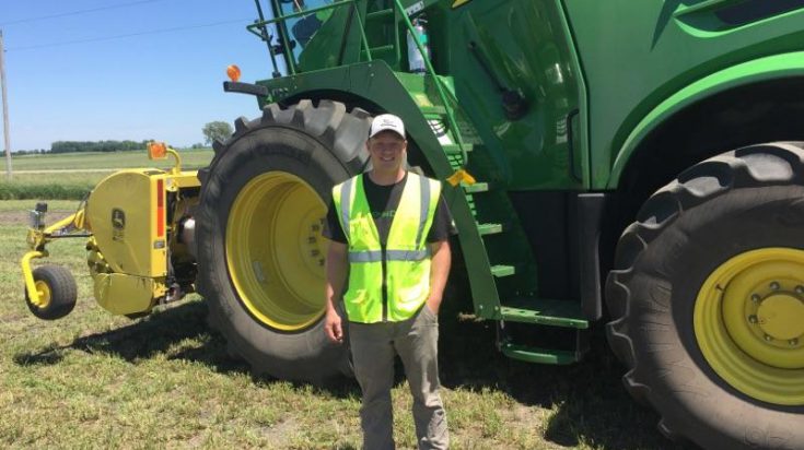 Male Ag student wearing a yellow safety vest standing in from of a John Deere combine