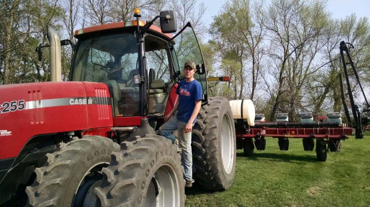 Male Agriculture student standing on the step of a red CASE tractor with a planter attached.