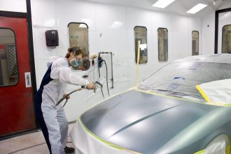 Auto body student suited up painting on a car in a paint booth