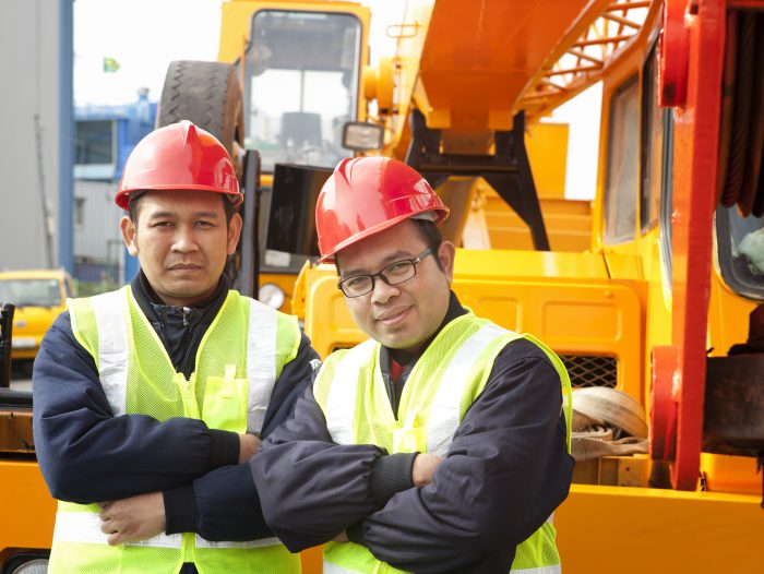 Construction workers posing next to the huge mobile crane
