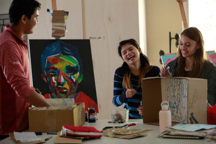 2 young female and 1 young male art students in art class smiling and laughing