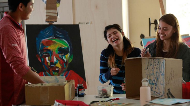 2 young female and 1 young male art students in art class smiling and laughing