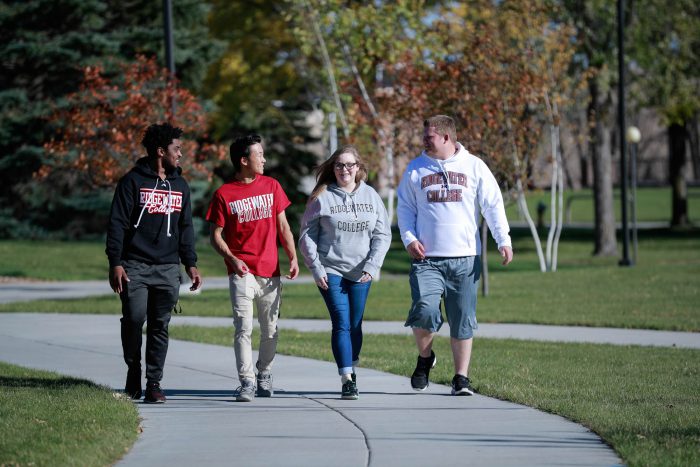 Four students, three male and one female, walk on a campus sidewalk