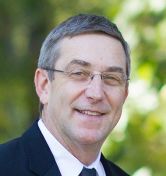 Headshot for Tom Bipes in a suit and glasses