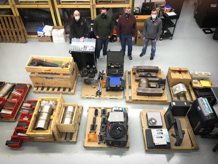 Photo of four men standing behind a lot of equipment.