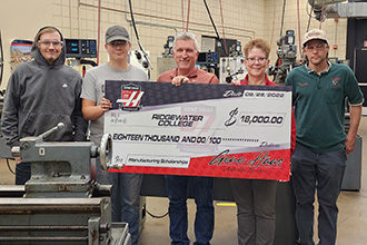 Machine Tool students Jamison Bever and Wayne Heller (on left) join instructor Greg Ryder (center), Hope Riska from the Gene Haas Foundation, and instructor Tom Meuleners (far right) to celebrate the generosity.