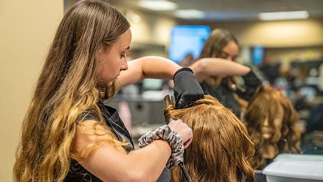 Cosmetology student curling a mannequin's hair with a curling iron.