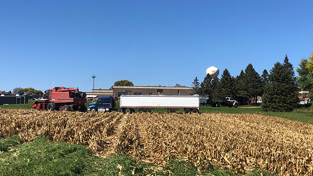 combine and semi truck on Willmar school's farm/field. Can see the school in the background as well as the water tower with the Ridgewater logo