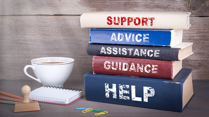 photo of a stack of books with the spines reading "support, advice, assistance, guidance, and help" with a tea cup and small notebook. Like is shining in the top left.